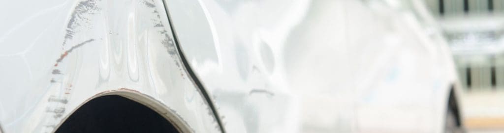 Close-up of a white car with visible scratches and dents on the fender, highlighting the impact of vandalism and overnight damage at dealerships. AI-powered security solutions can help prevent costly repairs and theft.