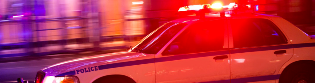 A police car with flashing red and blue emergency lights speeds through a city at night, symbolizing rapid law enforcement response. The image highlights the importance of video-verified alarms in reducing false alerts and ensuring faster police intervention for businesses and commercial properties.